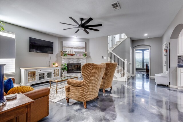 living room featuring arched walkways, ceiling fan, a fireplace, visible vents, and stairway