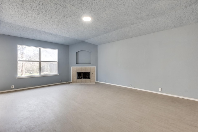 unfurnished living room featuring a tile fireplace, a textured ceiling, baseboards, and wood finished floors