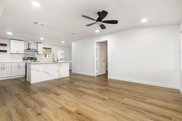 kitchen with a kitchen island with sink, visible vents, white cabinetry, wall chimney range hood, and open shelves