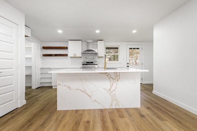 kitchen with a kitchen island with sink, stainless steel electric range oven, wall chimney range hood, and open shelves