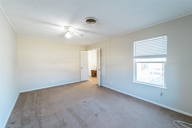 empty room with a textured ceiling, carpet flooring, visible vents, baseboards, and ornamental molding