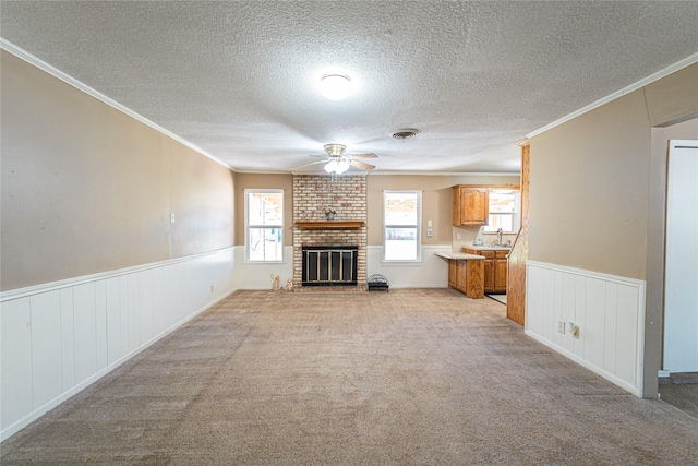 unfurnished living room featuring light carpet, a wainscoted wall, a brick fireplace, and crown molding