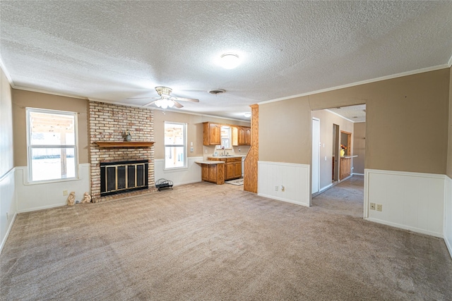 unfurnished living room with light carpet, a brick fireplace, a wealth of natural light, and wainscoting