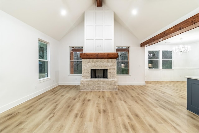 unfurnished living room featuring light wood-style flooring, beam ceiling, a brick fireplace, high vaulted ceiling, and a notable chandelier