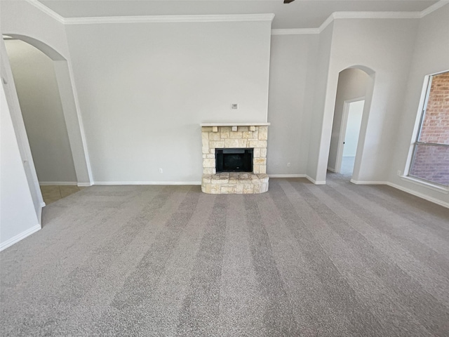 unfurnished living room with carpet floors, baseboards, ornamental molding, and a stone fireplace