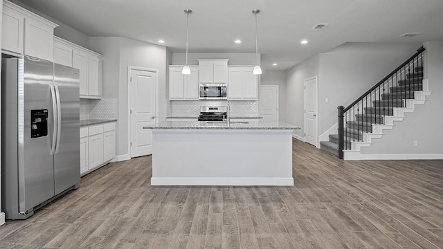 kitchen featuring pendant lighting, stainless steel appliances, a center island with sink, and white cabinets