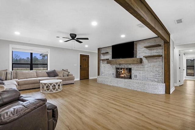 living room featuring ornamental molding, a brick fireplace, visible vents, and light wood finished floors