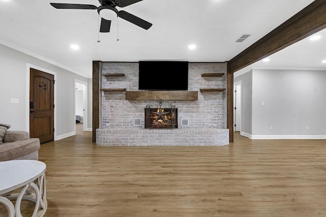 living room with a fireplace, light wood finished floors, visible vents, ornamental molding, and baseboards