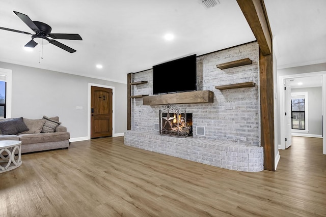 living room featuring a fireplace, visible vents, wood finished floors, and ornamental molding