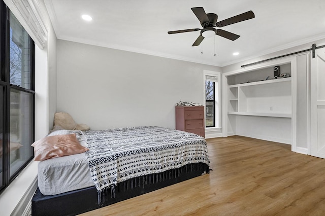 bedroom featuring ornamental molding, wood finished floors, ceiling fan, and a barn door