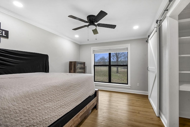 bedroom featuring a barn door, crown molding, baseboards, and wood finished floors