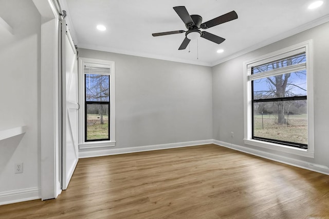 empty room featuring ornamental molding, a barn door, wood finished floors, and baseboards