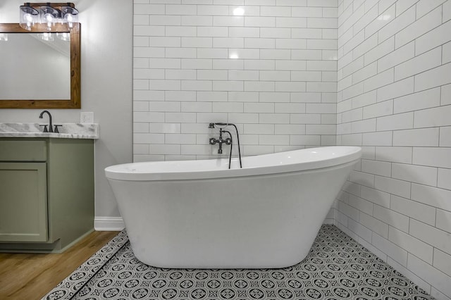 bathroom featuring a freestanding bath, wood finished floors, vanity, and tile walls