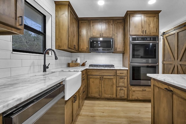 kitchen with light stone counters, stainless steel appliances, light wood-style flooring, decorative backsplash, and a barn door