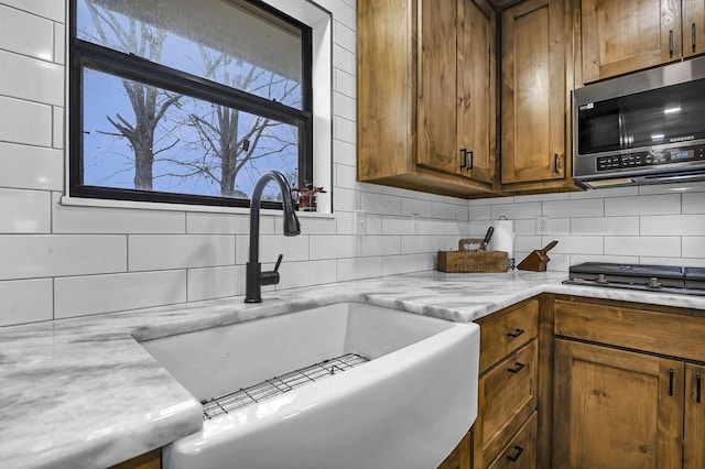 kitchen featuring light stone counters, brown cabinets, decorative backsplash, appliances with stainless steel finishes, and a sink