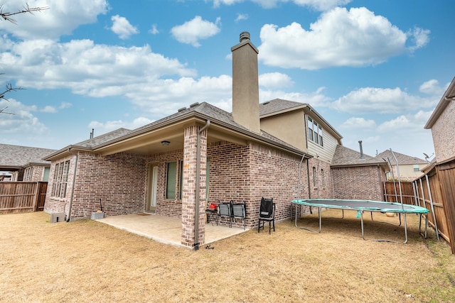 back of house featuring a patio, a fenced backyard, a chimney, a trampoline, and brick siding