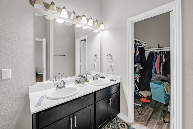 bathroom featuring a walk in closet, wood finished floors, a sink, and double vanity