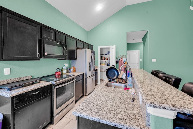 kitchen featuring an island with sink, lofted ceiling, stainless steel appliances, a kitchen bar, and a sink