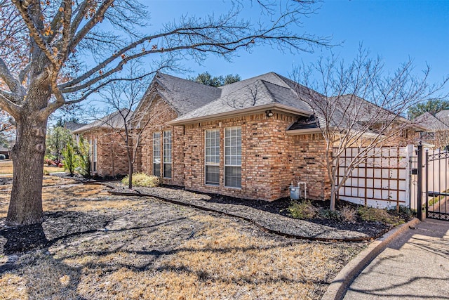 view of side of home with a shingled roof, a gate, and brick siding