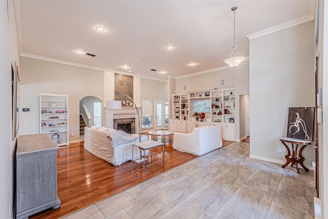 living room featuring arched walkways, a large fireplace, visible vents, light wood-style floors, and crown molding