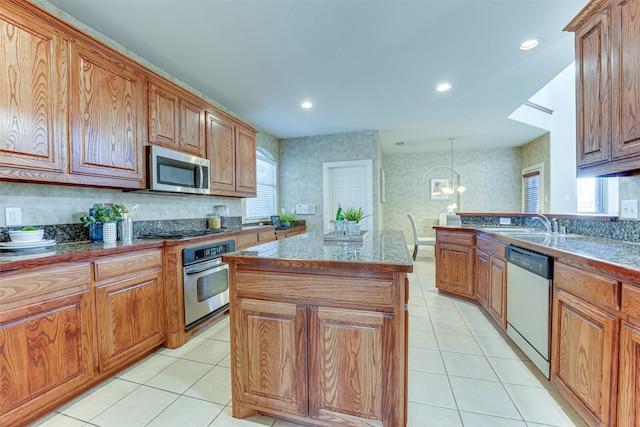 kitchen with light tile patterned floors, stainless steel appliances, a kitchen island, brown cabinetry, and wallpapered walls