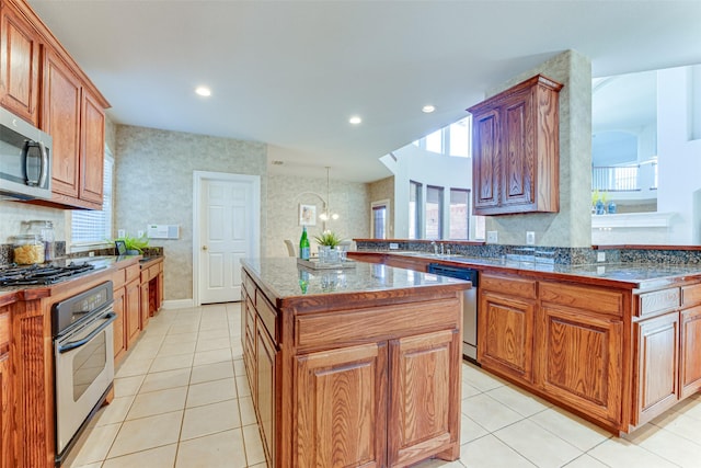 kitchen with stainless steel appliances, brown cabinetry, light tile patterned flooring, and a kitchen island