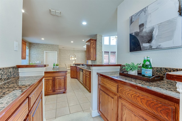 kitchen with brown cabinetry, visible vents, stainless steel dishwasher, and light tile patterned floors