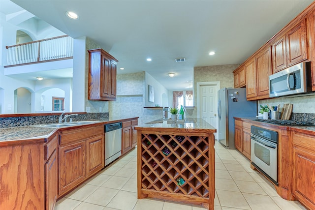 kitchen featuring stainless steel appliances, a center island with sink, a sink, and light tile patterned floors