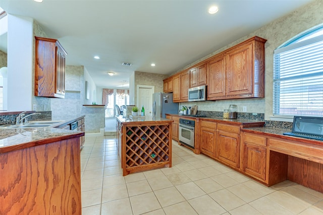 kitchen with a center island, brown cabinets, light tile patterned floors, stainless steel appliances, and a sink