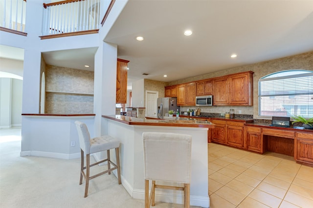 kitchen with a breakfast bar area, brown cabinets, a peninsula, stainless steel appliances, and recessed lighting