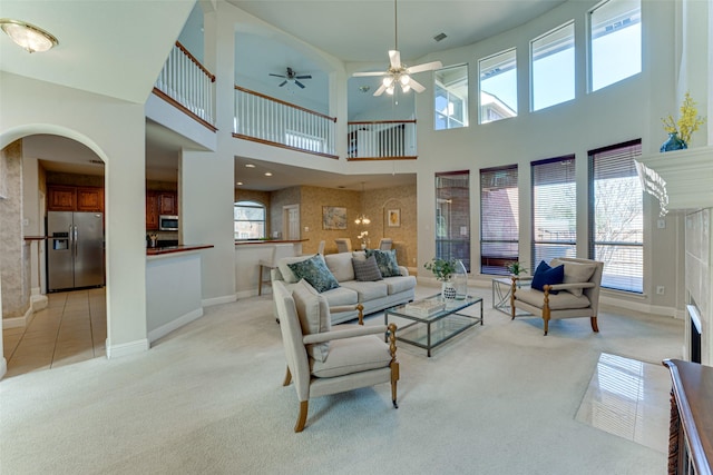 living room with ceiling fan, baseboards, arched walkways, and light colored carpet