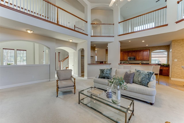 living area featuring light tile patterned floors, baseboards, light colored carpet, ceiling fan, and stairway