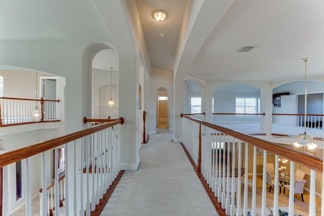 hallway featuring an upstairs landing, visible vents, baseboards, and light colored carpet