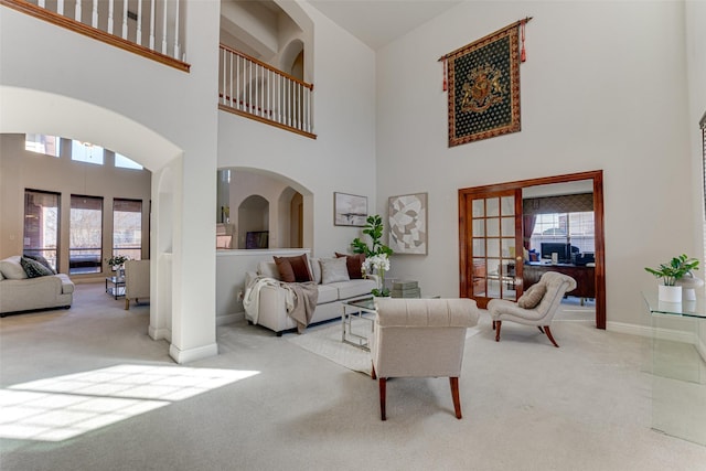 living area with arched walkways, light carpet, and baseboards