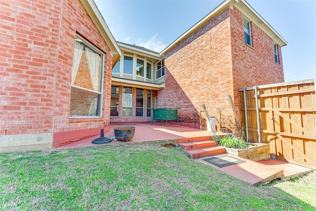 rear view of house featuring brick siding, a lawn, a patio area, and fence