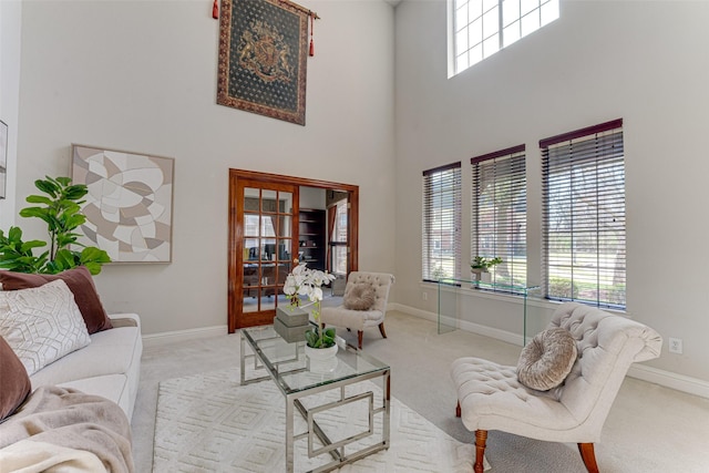 living area with a high ceiling, light carpet, and baseboards