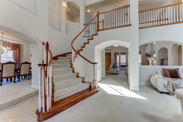 foyer entrance featuring arched walkways, stairway, an inviting chandelier, light carpet, and baseboards