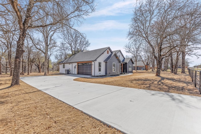 view of side of home with an attached garage, central AC, a yard, driveway, and board and batten siding