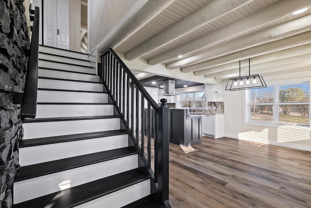 staircase featuring beamed ceiling, baseboards, and wood finished floors