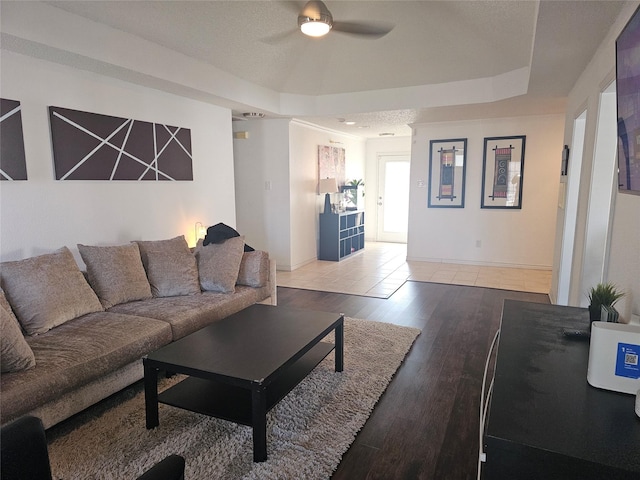 living area featuring ceiling fan, a tray ceiling, wood finished floors, and baseboards