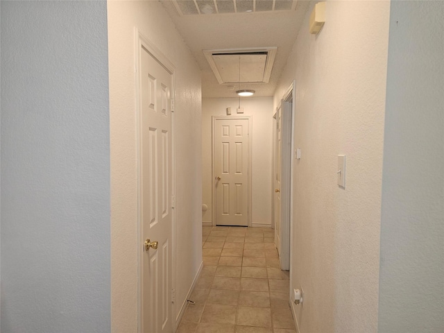 corridor with light tile patterned floors, attic access, visible vents, and baseboards