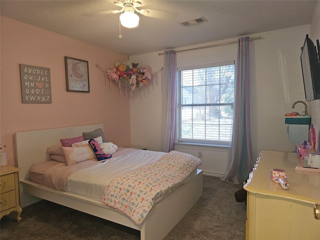 bedroom with a ceiling fan, dark colored carpet, visible vents, and a textured ceiling