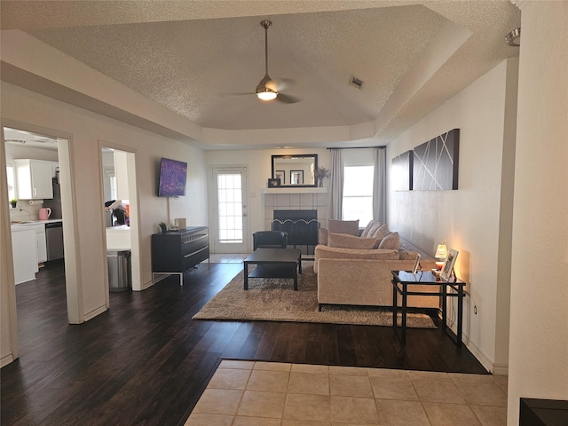 living room featuring a textured ceiling, wood finished floors, a fireplace, and a raised ceiling