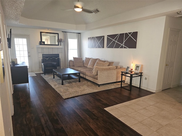 living room featuring a textured ceiling, a tray ceiling, wood finished floors, and a tiled fireplace