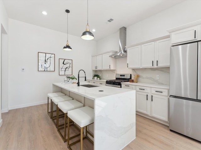 kitchen with a center island with sink, wall chimney exhaust hood, stainless steel appliances, white cabinetry, and a sink