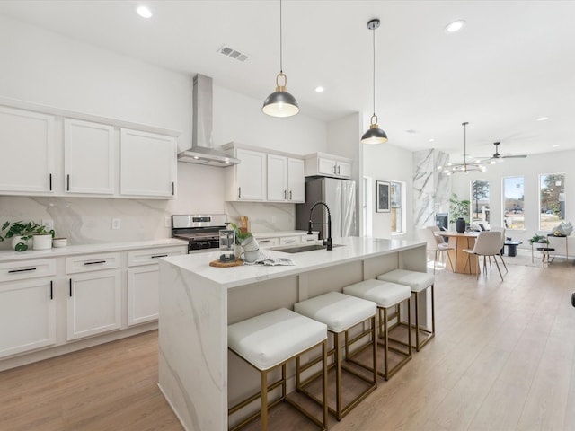 kitchen with decorative light fixtures, stainless steel appliances, visible vents, a kitchen island with sink, and wall chimney range hood