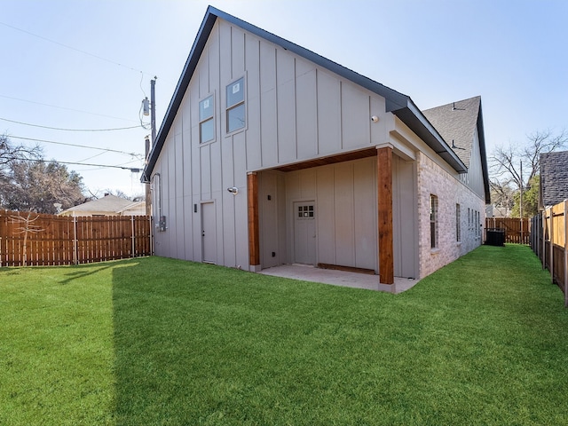 rear view of house with board and batten siding, a fenced backyard, a lawn, and brick siding