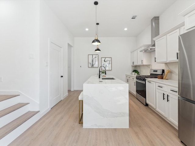 kitchen featuring a center island with sink, stainless steel appliances, hanging light fixtures, white cabinetry, and a sink