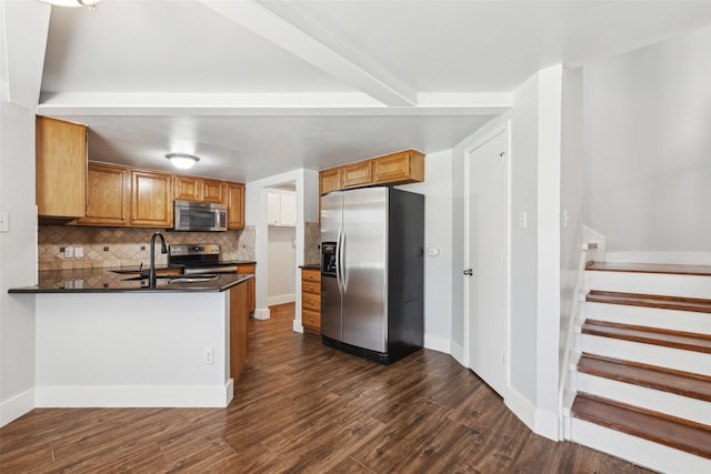 kitchen with dark wood-style flooring, appliances with stainless steel finishes, brown cabinetry, a sink, and a peninsula