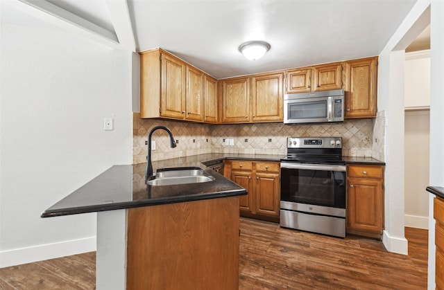 kitchen with dark wood-style flooring, stainless steel appliances, decorative backsplash, a sink, and a peninsula